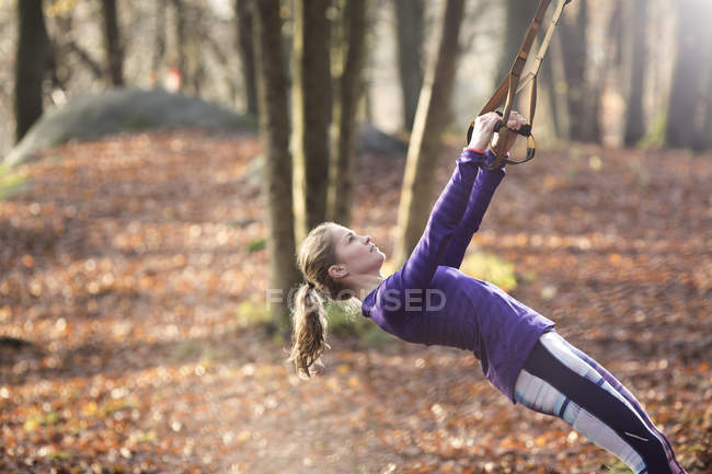 Вид сбоку на молодую женщину в лесу, откинутую назад с помощью резиновых лент, смотрящую вверх — стоковое фото