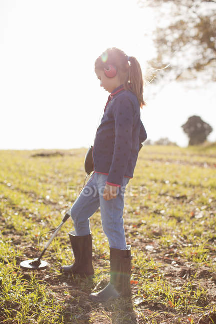 Girl wearing headphones using metal detector in field — Stock Photo