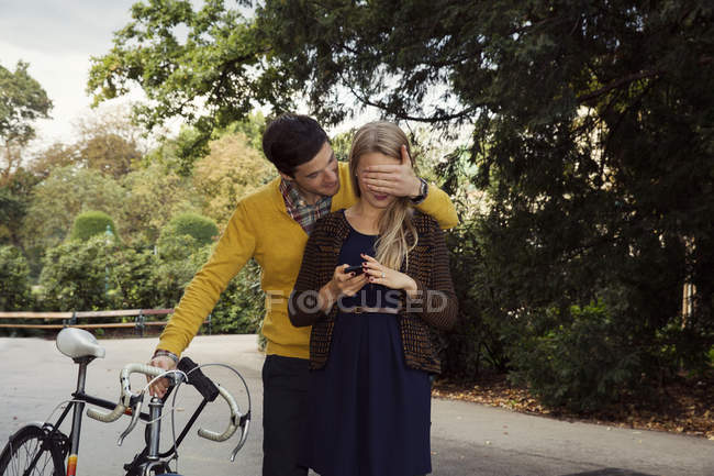 Jovem homem cobrindo namorada olhos no parque — Fotografia de Stock