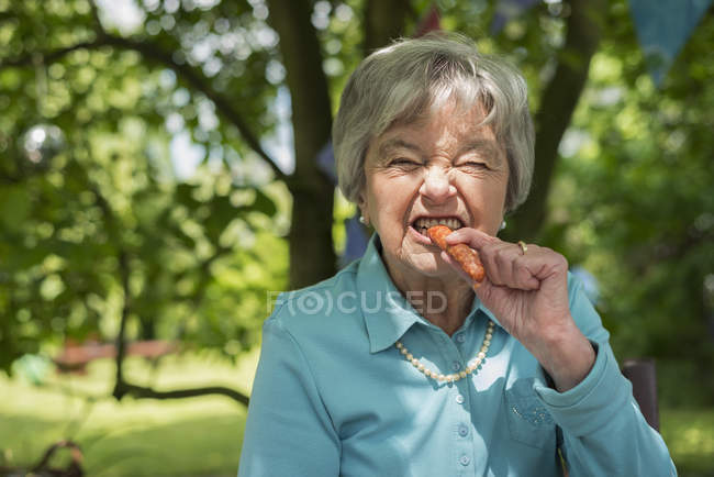 Senior mulher mordendo salsicha no jardim — Fotografia de Stock
