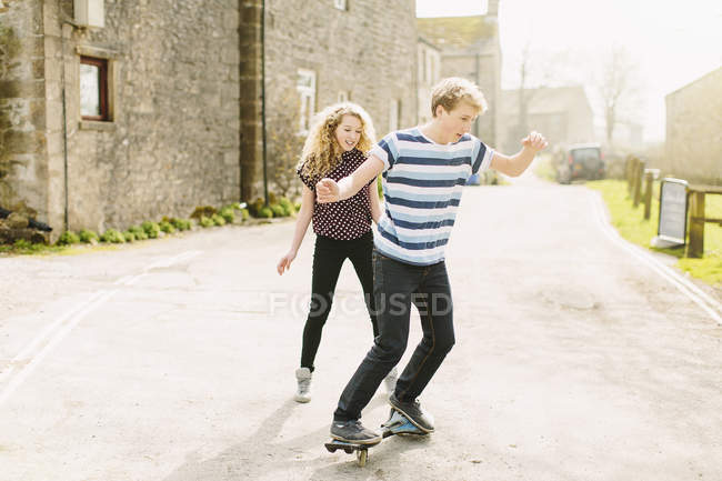 Подростковый брат и сестра катаются на скейтборде по сельской дороге — стоковое фото