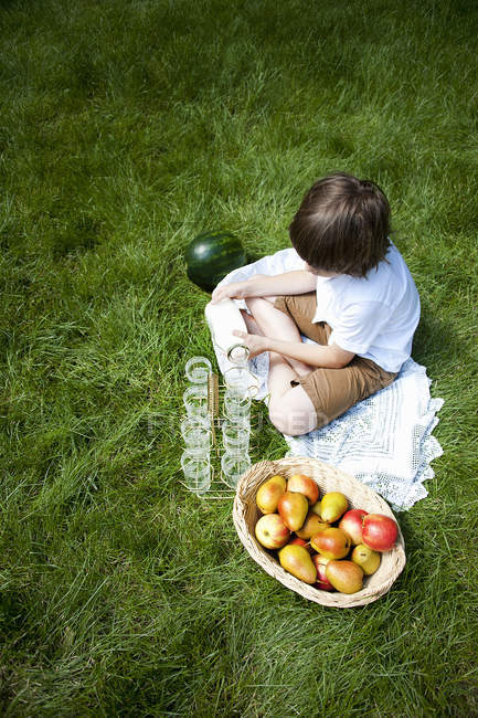 Overhead view of boy cross legged on grass pouring milk into glasses — Stock Photo