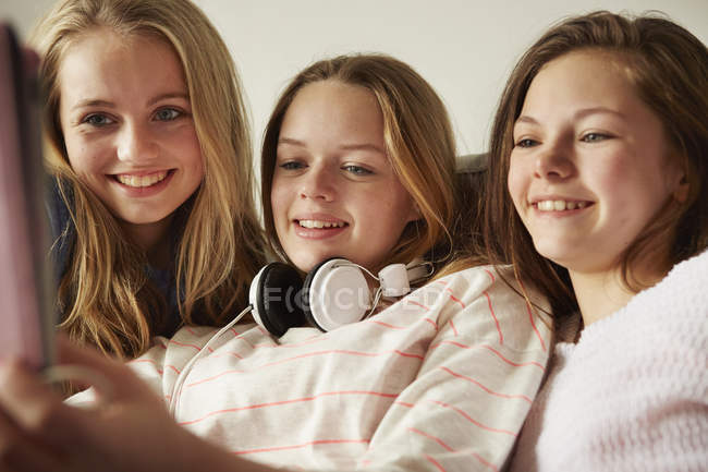 Три дівчини на дивані використовують цифровий планшет — стокове фото