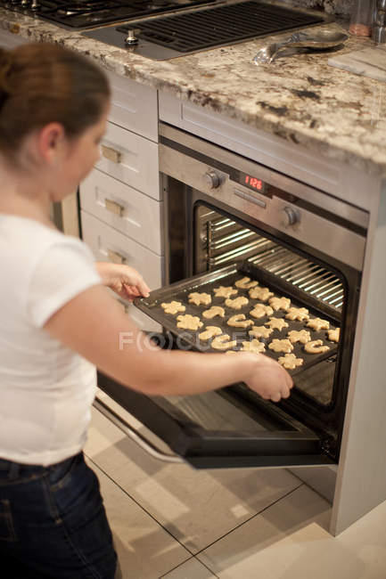Teenage girl placing baking tray of biscuits in oven — Stock Photo