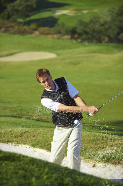 Golfista che prende l'oscillazione di golf nella trappola di sabbia, pallina da golf a mezz'aria — Foto stock