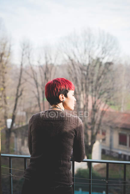 Jovem encostada contra grades de varanda, olhando para a vista — Fotografia de Stock