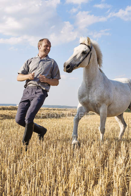 Male trainer running in front of white horse in field — Stock Photo