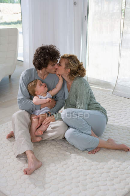 Padres besándose, bebé mirando - foto de stock