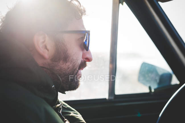 Gros plan d'un homme adulte portant des lunettes de soleil dans une voiture éclairée par le soleil — Photo de stock
