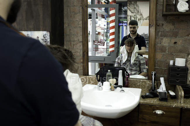Espejo imagen del joven y peluquero en la barbería - foto de stock