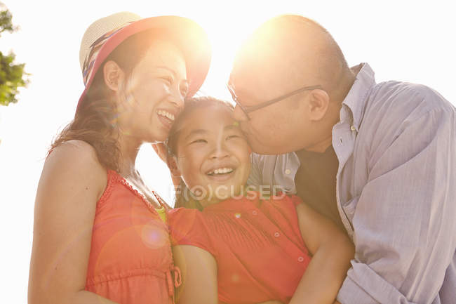 Батьки цілують дочку на щоці на сонячному світлі — стокове фото