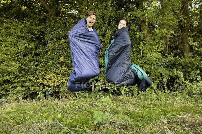 Casal jovem pulando no ar em seus sacos de dormir — Fotografia de Stock