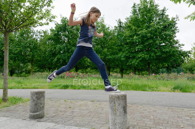 Girl jumping bollards mid air in park — Stock Photo