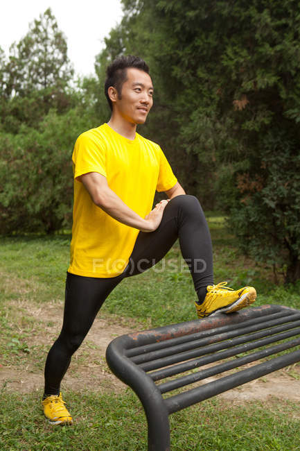 Junge Läuferin streckt Bein auf Parkbank im Park — Stockfoto
