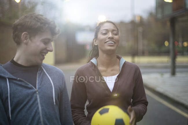 Jovem e mulher caminhando na rua, segurando futebol — Fotografia de Stock
