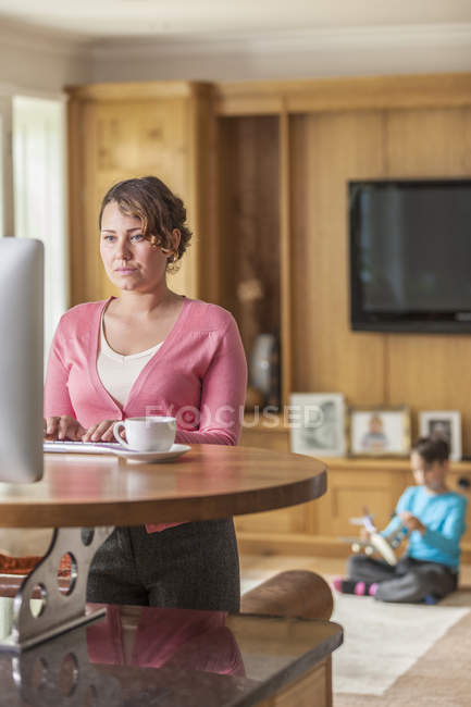 Mère adulte moyenne travaillant sur ordinateur pendant que son fils joue — Photo de stock
