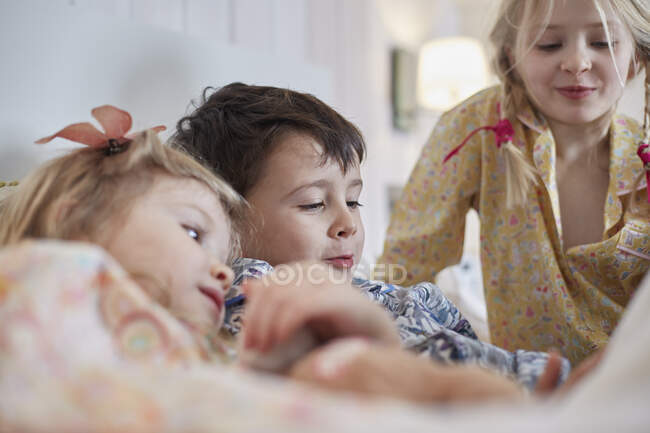 Niños en pijama en la cama - foto de stock
