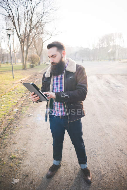 Giovane uomo barbuto utilizzando tablet digitale nel parco — Foto stock