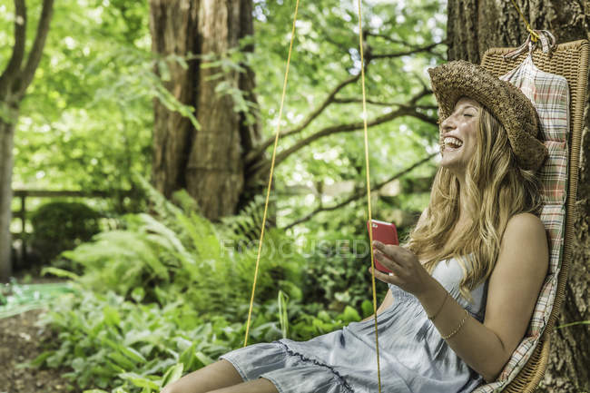 Молода жінка, сидячи на садовому сидінні, сміється — стокове фото