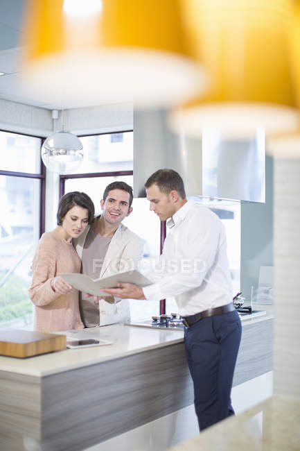 Mid adult couple and salesman looking at brochure in kitchen showroom — Stock Photo