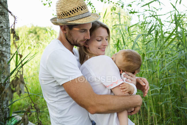 Mid adult couple and baby daughter with arms around each other in reeds — Stock Photo