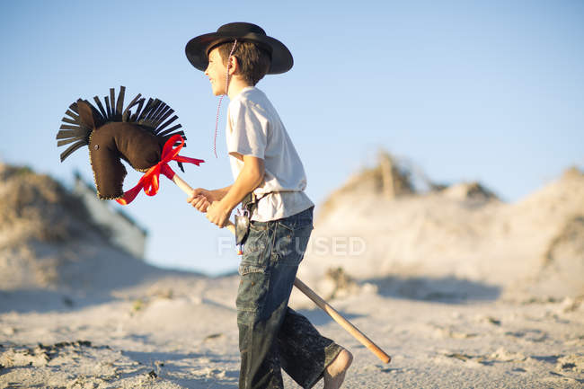 Boy with hobby horse dressed as cowboy in sand dunes — Stock Photo
