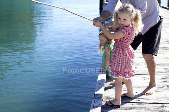 Человек и дочери рыбачат с пирса, Новая Зеландия — стоковое фото