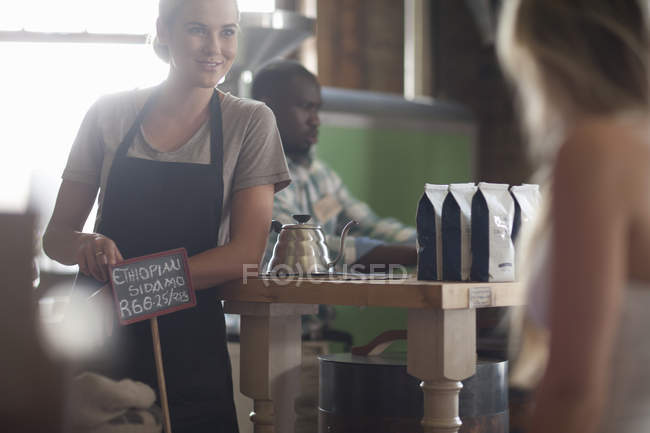 Молода жінка офіціантка консультує з питань вибору кави в кафе — стокове фото