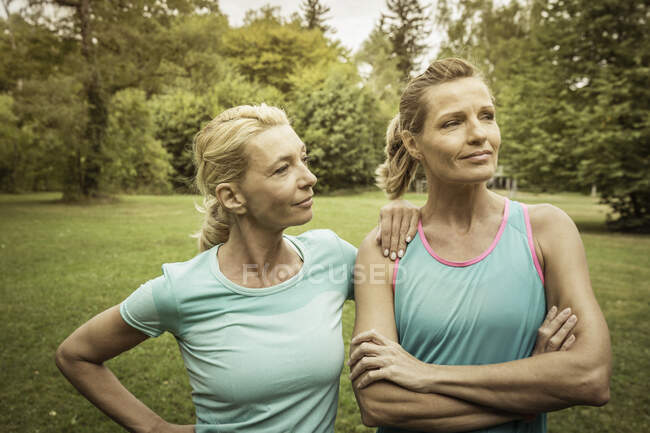 Mujeres maduras en el parque llevando ropa deportiva brazos cruzados mirando hacia otro lado - foto de stock