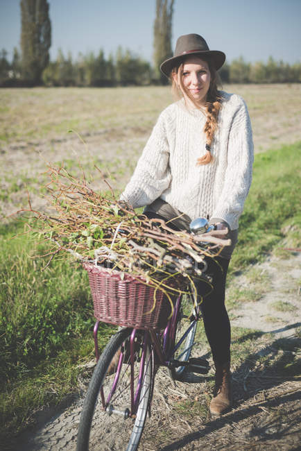Young woman carrying bunch of sticks on bicycle — Stock Photo