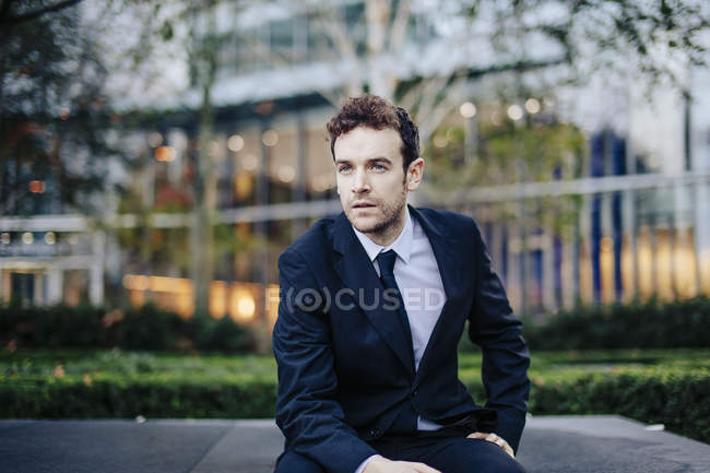 Homme d'affaires assis sur un mur devant un immeuble de bureaux — Photo de stock