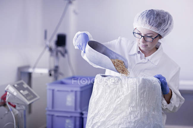 Factory worker scooping food into sack — Stock Photo