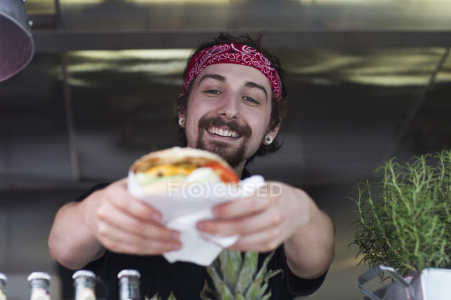 Молодой человек подает гамбургер из фургона быстрого питания — стоковое фото