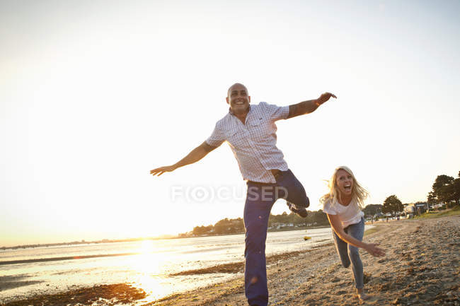 Couple having fun on sunny beach at sunset — Stock Photo