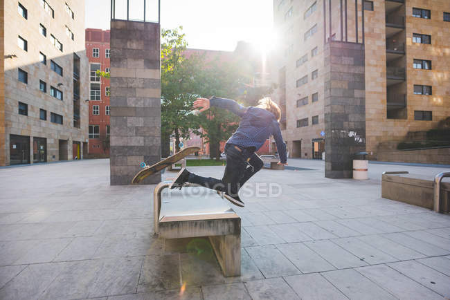 Young male skateboarder falling head first whilst skateboarding on urban concourse seat — Stock Photo