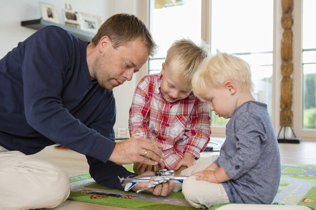 Hombre adulto medio y dos hijos preparando avión de juguete en el piso de la sala de estar - foto de stock