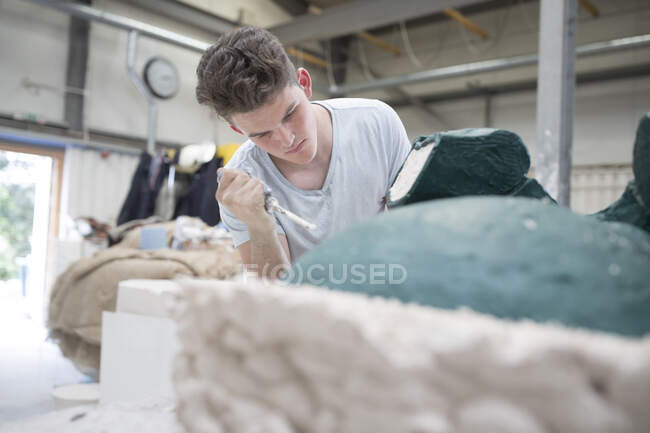 Молодий чоловік, працівник ливарної справи, знімає плісень з бронзової скульптури з бронзової ливарні. — стокове фото