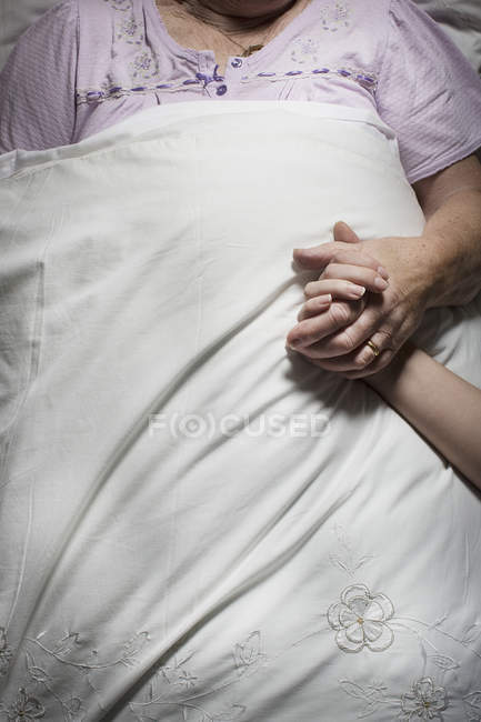 Imagens cortadas de mulher jovem segurando dormindo sênior mão feminina — Fotografia de Stock