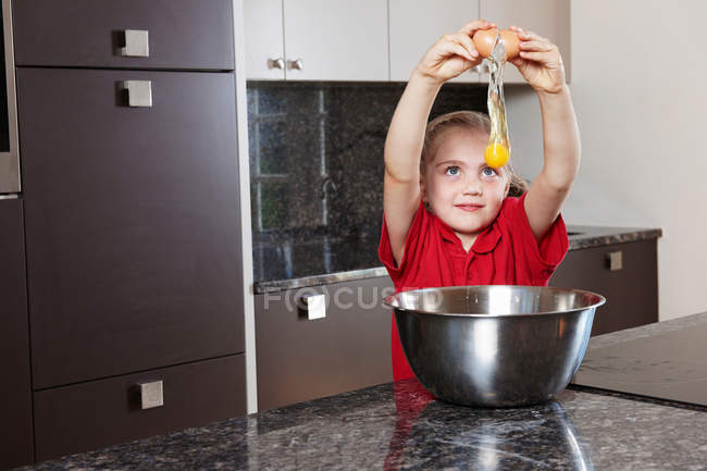 Chica agrietando huevo sobre cuenco - foto de stock