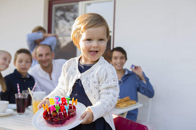 Female toddler carrying birthday cake on patio — Stock Photo
