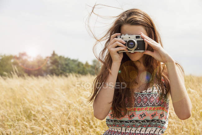 Jovem mulher tirando foto com câmera vintage no campo — Fotografia de Stock