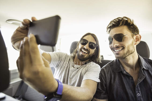 Друзі на задньому сидінні автомобіля в сонцезахисних окулярах приймають селфі — стокове фото