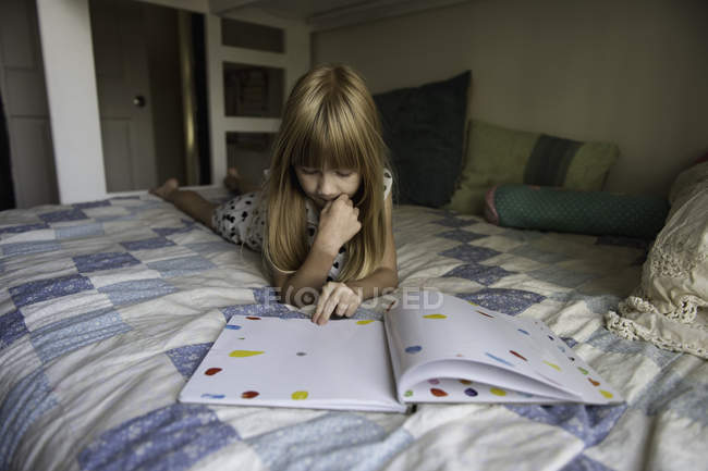 Young girl laying on bed reading book — Stock Photo