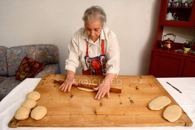 Older woman rolling dough on board — Stock Photo