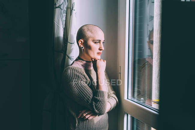 Portrait of young woman with shaved head gazing through window — Stock Photo