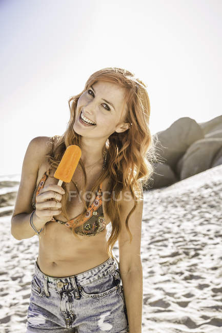 Ritratto di donna con lunghi capelli rossi che mangia ghiacciolo in spiaggia, Città del Capo, Sud Africa — Foto stock
