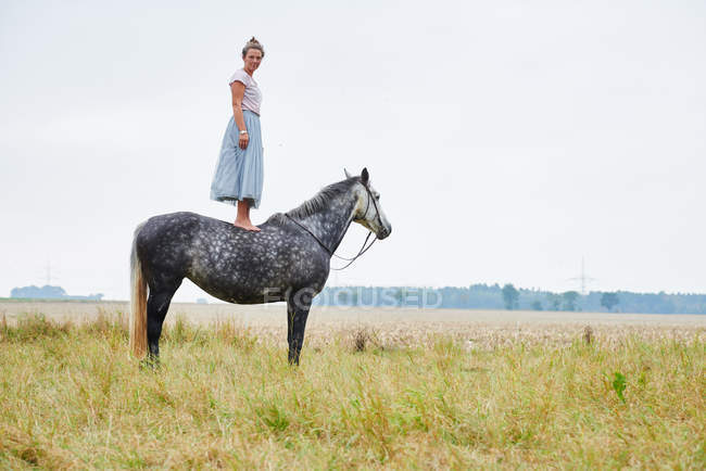 Женщина в юбке, стоящая на вершине серой лошади в поле — стоковое фото