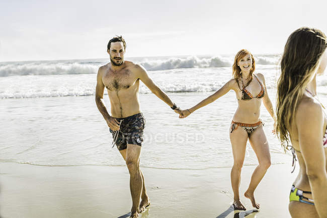 Mid adult couple wearing bikini and swimming shorts holding hands at beach, Cape Town, South Africa — Stock Photo