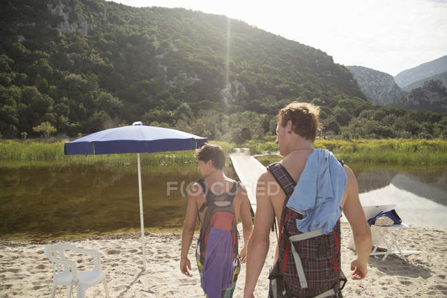 Rear view of young men carrying backpacks on beach, Cala Luna, Sardinia, Italy — Stock Photo