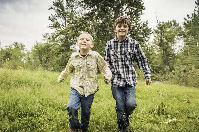 Vista frontal de chicos corriendo en el campo mirando a la cámara sonriendo - foto de stock